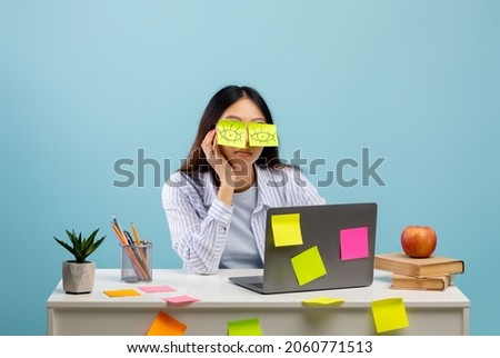 A lot of work concept. Tired asian female student sleeping with stickers on eyes, sitting at table over blue studio background. Distracted woman at home office Royalty-Free Stock Photo #2060771513