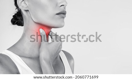 Closeup of sick woman having sore throat, touching her neck with red inflamed zone, suffering from laryngeal disorder, tonsillitis, throat cancer, cold, free copy space over gray studio background Royalty-Free Stock Photo #2060771699