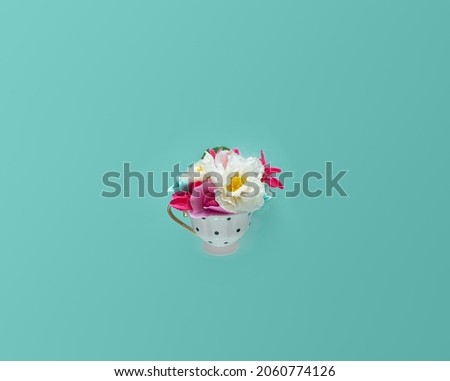 Vintage, polka dots patterned tea cup full of colorful, exotic, summer flowers, against turquoise background. Good morning minimal creative layout. Fresh healthy breakfast and aromatic drink. 