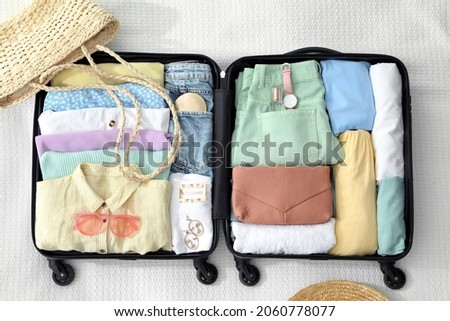 Open suitcase packed for trip and accessories on white blanket, flat lay Royalty-Free Stock Photo #2060778077