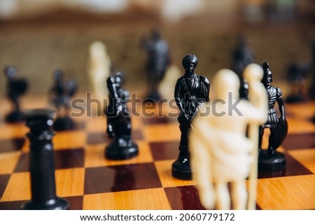 Chess white and black pieces fight on battlefield for their king. Hand moves chess piece