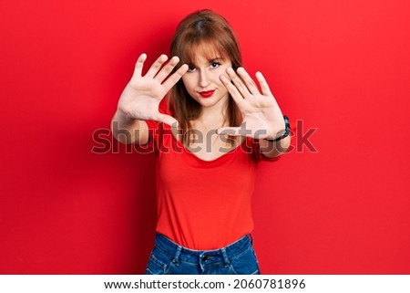 Redhead young woman wearing casual red t shirt doing frame using hands palms and fingers, camera perspective 