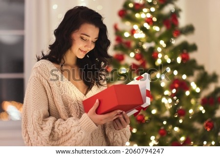 Curious happy romantic woman standing against Christmas tree background. Cheerful lady surprised of the present after the opening in the gift box. Marry Christmas and Happy Holidays Royalty-Free Stock Photo #2060794247