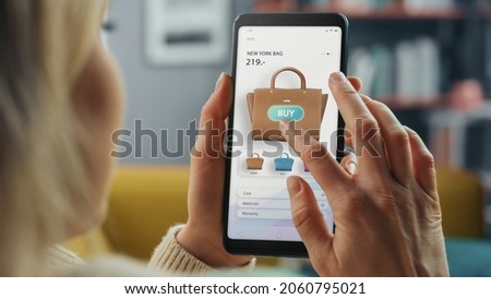 Beautiful Caucasian Female is Using Smartphone with Clothing Online Web Store to Choose and Buy Handbag from New Collection. Female Surfing the Net and Lying on Couch Sofa at Home Living Room. Royalty-Free Stock Photo #2060795021