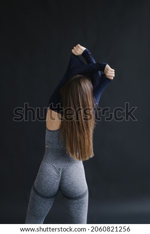 Sports inspiration and mood picture. Stylish woman takes off her sportswear after training. Black background. Anatomical leggings with embossed buttocks. Aerobics and stretching coach. Fit chick