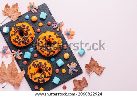 Pumpkin and chocolate doughnuts, Halloween lollipops, gummy candy and marshmallows on pink - Halloween candy flat lay on pink table, top view