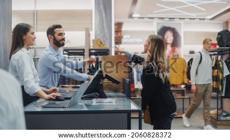Clothing Store Checkout Cashier Counter: Beautiful Young Woman Buys Blouse from Friendly Retail Sales assistant, Receiving Bag with Purchases. Trendy Fashion Shop with of Designer Brands Royalty-Free Stock Photo #2060828372