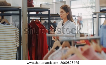 Clothing Store: Businesswoman and Visual Merchandising Specialist Uses Smartphone To Create Stylish Collection. Fashion Shop Sales Retail Manager Checks Stock. Small Business Owner and Designer Works