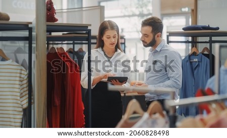 Clothing Store: Businesswoman Uses Tablet Computer, Talks to Visual Merchandising Specialist, Collaborate To Create Stylish Collection. Small Business Fashion Shop Sales Manager Talks to Designer Royalty-Free Stock Photo #2060828498