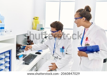 Man and woman wearing scientist uniform using computer working at laboratory