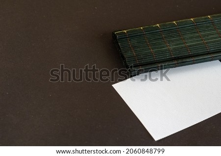 Dark green bamboo table cloth and white rectangle opposite black background. Plastic blank textured card. Selective Focus.