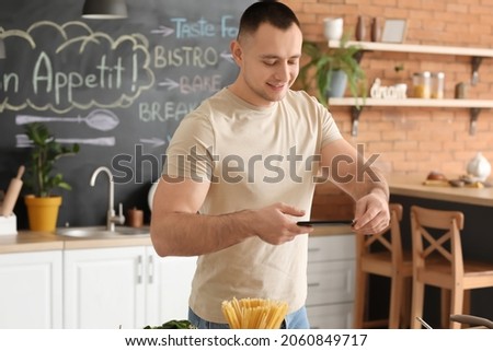 Young man taking photo of baked fish with vegetables in kitchen