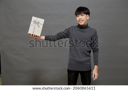 Christmas party and holidays concept. young Asian man holding gift box studio shot, Isolated on gray background