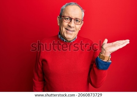 Handsome senior man with grey hair wearing casual clothes and glasses smiling cheerful presenting and pointing with palm of hand looking at the camera. 