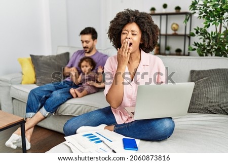 Mother of interracial family working using computer laptop at home bored yawning tired covering mouth with hand. restless and sleepiness. 