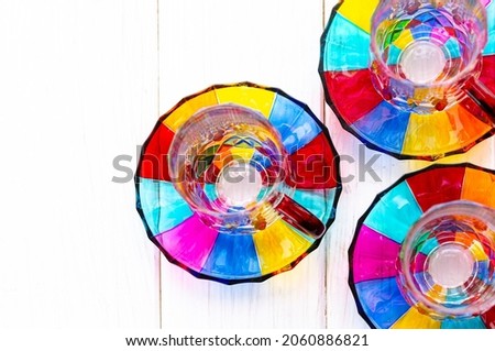 Multi-colored glass cups and saucers for coffee and tea stand on a wooden tray on the window sill