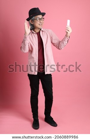 The senior Asian man standing on the pink background.