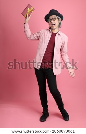 The senior Asian man standing on the pink background.