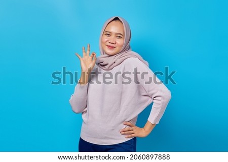 portrait of beautiful asian woman smiling doing okay sign with hand on blue background