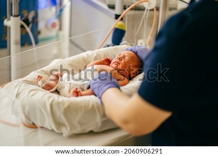 Unrecognizable nurse in blue gloves takes action and care for premature baby, selective focus on baby eye Newborn is placed in the incubator. Neonatal intensive care unit Royalty-Free Stock Photo #2060906291