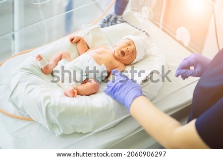 Unrecognizable nurse in blue gloves takes action and care for premature baby, selective focus on baby eye Newborn is placed in the incubator. Neonatal intensive care unit Royalty-Free Stock Photo #2060906297