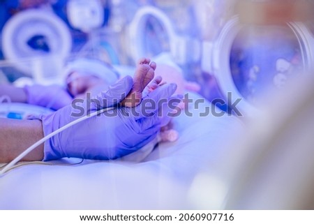 Macro photo of doctor's hands and legs of a child. Newborn is placed in a medical incubator under ultraviolet lamp. Neonatal intensive care unit. Royalty-Free Stock Photo #2060907716