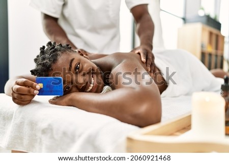 African american woman smiling happy reciving back massage and holding credit card at the clinic.