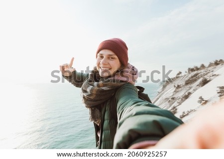 Happy woman traveler makes selfie on the background of the sea and sky. She is inspired and free. The weather is cold and sunny.