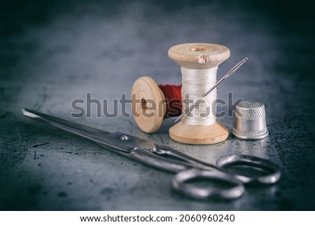 Multicolored threads on a wooden spool, sewing needle with scissors thimble and tailor's tape on an old surface. Sewing thread background. Retro style
