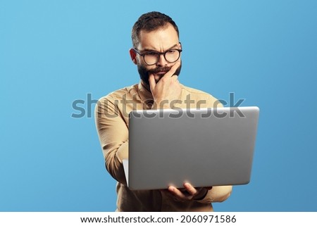 Portrait of a doubtful bearded man holding laptop computer isolated over blue background  Royalty-Free Stock Photo #2060971586