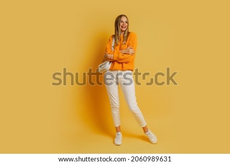 Pretty   blond  woman  in   trendy autumn outfit   posing on yellow background in studio.  Holding  white leather bag.  Full lenght. 
