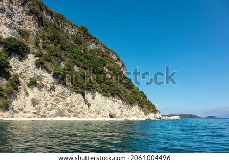 Scenic white pebble beach in blue water of Ionian Sea with green cliffs and bright sky. Nature of Lefkada island in Greece. Summer travel destination