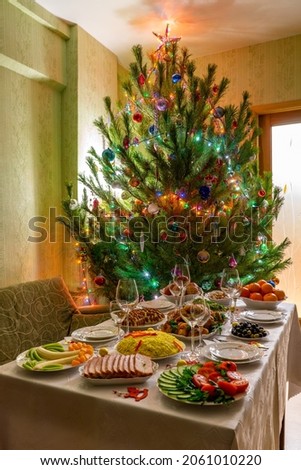 Festive Christmas served table against beautiful green pine tree decorated with many colorful new year toys. Xmas dinner, delicious food, christmas turkey. Winter holidays celebration at cozy home Royalty-Free Stock Photo #2061010220