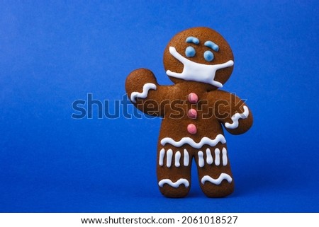 Gingerbread man with protective medical mask standing on blue background.