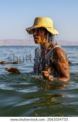 black woman bathing in sea of galilee srael. water dripping and splashing as she enjoys lake tiberius and sun.