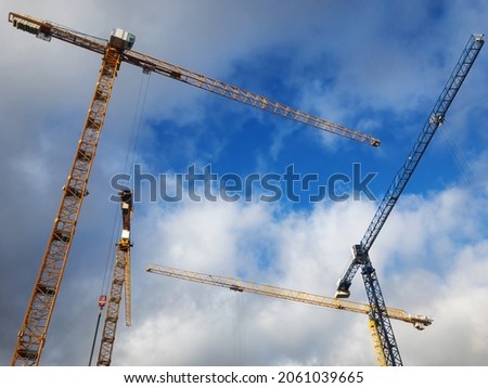 Group of tower cranes on the construction site against blue sky. Cranes for construction of high-rise buildings. Concept of urban development and architecturewith copy space for the text.