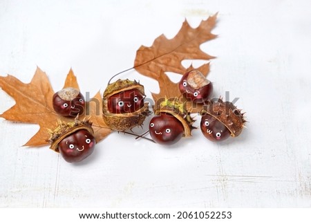 Chestnuts with cute smiling faces and autumn leaves on light grey background. DIY idea for fall season. chestnuts in form of mysterious living creatures, monsters. symbol of autumn