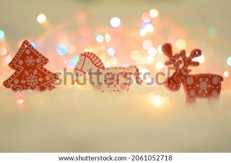 Wooden figures of a fir tree, a deer and a horse on a background of colorful Christmas lights. Red and white colors. Soft focus.
