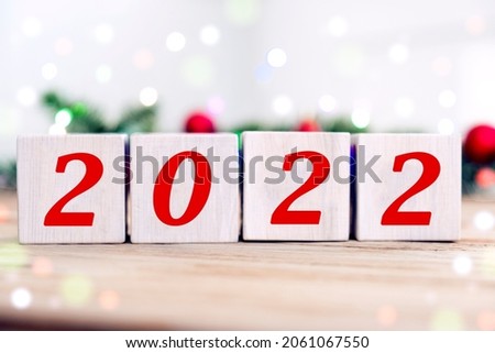 Happy New Year 2022 on wooden cube blocks with fir branches and blurred bokeh lights on the background. Greeting card for winter holidays and Merry Christmas.