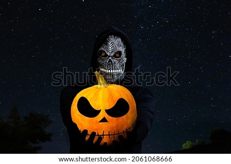 Grim reaper holding halloween pumpkin head. Man in death mask with fire flame in eyes on night sky starry background. Halloween holiday concept. Dark horror.
