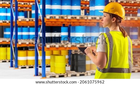 manager is counting chemical barrels. Metal barrels in front of warehouse worker. Manager in yellow uniform. Blurred racks in background. Work in chemical industry. Warehouse worker with tablet Royalty-Free Stock Photo #2061075962