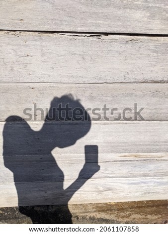 the shadow of a man taking a photo using a smartphone on a wooden wall in the hot sun during the day