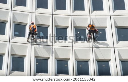 Two men rappelling from the wall for fix the damaged building in the city. Rappelling is a controlled descent off a vertical drop, such as a rock face, by descending a fixed rope. Royalty-Free Stock Photo #2061155342