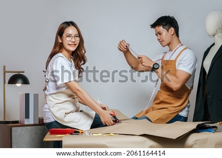Portrait Young handsome man and pretty woman, Couple fashion designer working with scissor cutting on paper clothing pattern at the studio at home