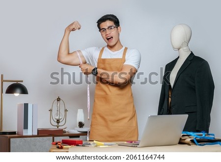 Portrait of young male fashion designer stylish smiile during working at fashion studio, Tailor man's taking measurements with measuring tape on his arm in studio at home