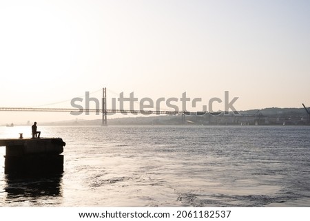 Panormic photo of the silhouette of a fisherman facing the river during sunset in Lisbon. Portugal