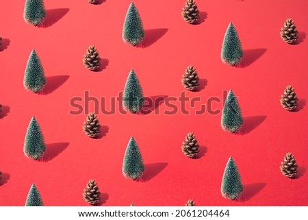 Arranged green New Year and Christmas tree with brown pinecone on a red pastel background. Pattern.