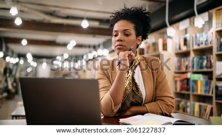 African American female professor using laptop while doing a research at university library. 