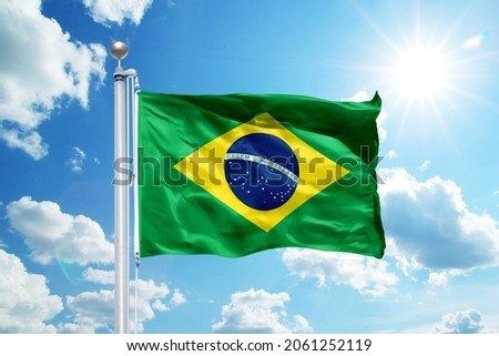 National Brazil flag waving in the wind, against the blue sky. Wavy flag in the sky with sunbeams. Royalty-Free Stock Photo #2061252119