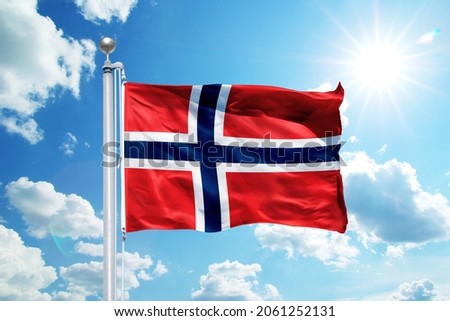 National Norway flag waving in the wind, against the blue sky. Wavy flag in the sky with sunbeams.